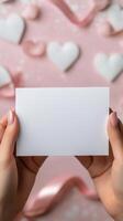 Hands holding a blank card above decorative hearts on a soft pink background photo