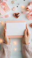 Hands holding a blank card above decorative hearts on a soft pink background photo