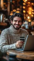 Smiling young man working on laptop in cozy cafe with credit card in hand photo