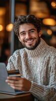 Smiling young man working on laptop in cozy cafe with credit card in hand photo
