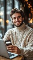 Smiling young man working on laptop in cozy cafe with credit card in hand photo