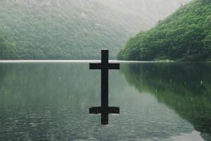 Reflection of a cross in calm water surrounded by mountains during early morning mist photo