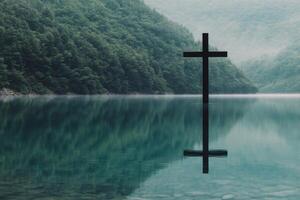 Reflection of a cross in calm water surrounded by mountains during early morning mist photo