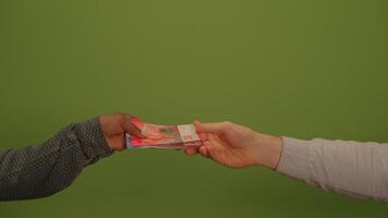 A hand holds a banknote before a vibrant green background, symbolizing finance and wealth video