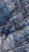 Aerial View reveals the intricate patterns of deep crevasses and textured ice on a Svinafellsjokull Glacier in Iceland. Vertical footage video