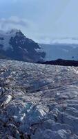 aéreo ver de un vasto glaciar con profundo azul fisuras rodeado por escabroso acantilados el luz de sol acentúa el contrastando texturas svinafellsjokull glaciar en Islandia. vertical imágenes video