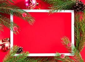Flat lay with Christmas tree, white horizontal frame and and Christmas decor on red background. Close up. Top view. Copy space. photo