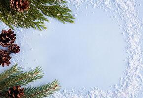 Christmas, New Year's or winter composition. Frame made of snow, fir branches and fir cones on blue background. New year greeting card. Flatlay. Top view. Copy space. photo