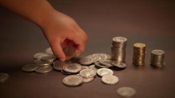 A young child is happily counting various coins spread out on a table in a playful manner video