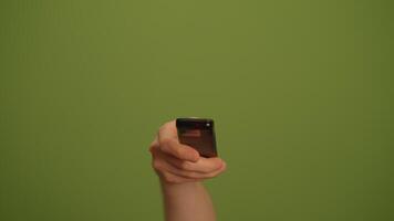 A hand is confidently holding a remote control in front of a vibrant green background video