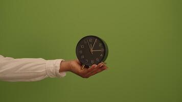 A hand holds a clock against a green background, symbolizing time management and design video