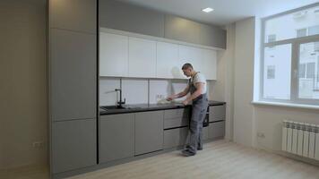 The builder checks the dimensions and quality of installation of the kitchen furniture structure. Professional worker in uniform in a new apartment. Production and installation of new furniture. video