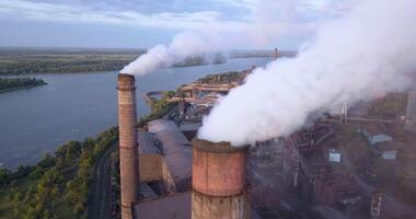 Industrial zone with a large pipe thick white smoke is poured from the factory pipe. Pollution of the environment. a pipe with smoke. Old factory near the river in Kamenskoye, Ukraine. Aerial view. video