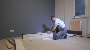 A builder in a work overalls is assembling a bed. Assembling furniture in a new apartment. video