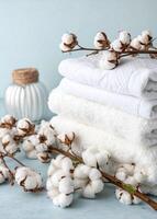 Stack of fluffy white towels adorned with cotton branches on a light blue background. photo