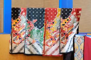 An array of Indonesian batik shirts and batik cloth hangs on the racks, displaying a variety of patterns and colors. photo