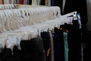 Thrifting's vibrant collection of sweaters, shirts, hoodies, trousers and knitted t-shirts are elegantly displayed on wooden hangers, featuring a variety of colors and textures. photo