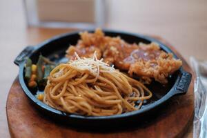 A delicious combination of crispy chicken and flavorful noodles served on a hot plate with vegetables. photo