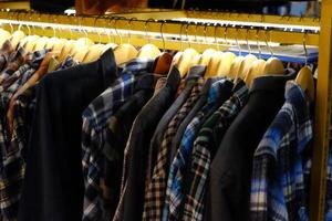 Thrifting's vibrant collection of sweaters, shirts, hoodies, trousers and knitted t-shirts are elegantly displayed on wooden hangers, featuring a variety of colors and textures. photo