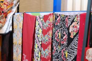 An array of Indonesian batik shirts and batik cloth hangs on the racks, displaying a variety of patterns and colors. photo