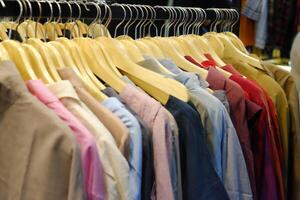 Thrifting's vibrant collection of sweaters, shirts, hoodies, trousers and knitted t-shirts are elegantly displayed on wooden hangers, featuring a variety of colors and textures. photo