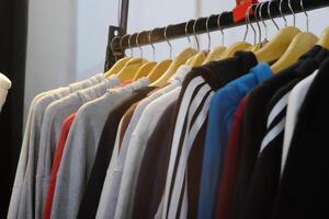 Thrifting's vibrant collection of sweaters, shirts, hoodies, trousers and knitted t-shirts are elegantly displayed on wooden hangers, featuring a variety of colors and textures. photo