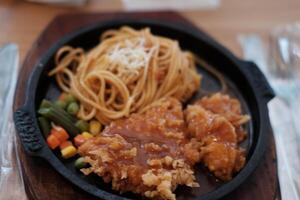 A delicious combination of crispy chicken and flavorful noodles served on a hot plate with vegetables. photo