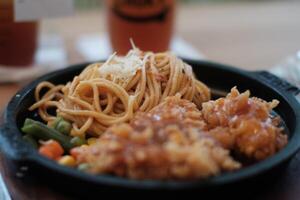 A delicious combination of crispy chicken and flavorful noodles served on a hot plate with vegetables. photo