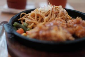 A delicious combination of crispy chicken and flavorful noodles served on a hot plate with vegetables. photo