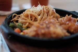 A delicious combination of crispy chicken and flavorful noodles served on a hot plate with vegetables. photo