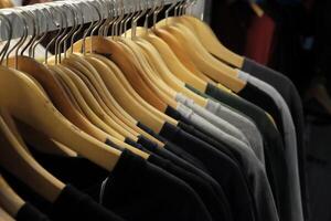 Thrifting's vibrant collection of sweaters, shirts, hoodies, trousers and knitted t-shirts are elegantly displayed on wooden hangers, featuring a variety of colors and textures. photo