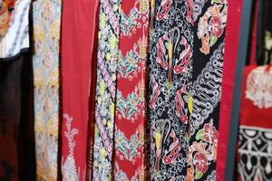 An array of Indonesian batik shirts and batik cloth hangs on the racks, displaying a variety of patterns and colors. photo