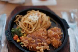 A delicious combination of crispy chicken and flavorful noodles served on a hot plate with vegetables. photo
