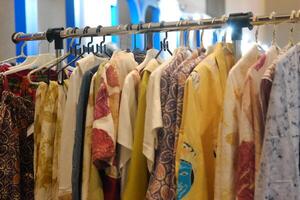 An array of Indonesian batik shirts and batik cloth hangs on the racks, displaying a variety of patterns and colors. photo
