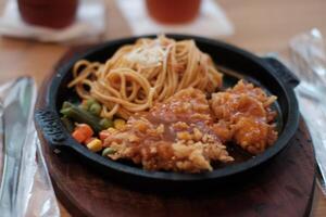 A delicious combination of crispy chicken and flavorful noodles served on a hot plate with vegetables. photo