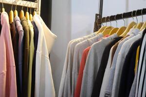 Thrifting's vibrant collection of sweaters, shirts, hoodies, trousers and knitted t-shirts are elegantly displayed on wooden hangers, featuring a variety of colors and textures. photo