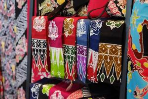 An array of Indonesian batik shirts and batik cloth hangs on the racks, displaying a variety of patterns and colors. photo
