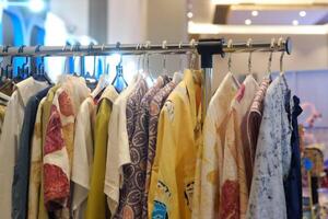 An array of Indonesian batik shirts and batik cloth hangs on the racks, displaying a variety of patterns and colors. photo