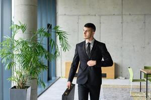 A determined businessman in a black suit confidently walks through the office, embodying professionalism and focus as he heads towards new challenges photo