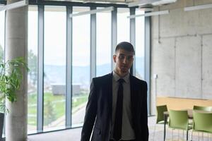 A determined businessman in a black suit confidently walks through the office, embodying professionalism and focus as he heads towards new challenges photo