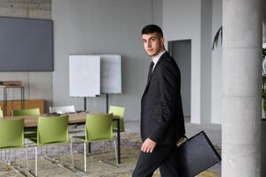 A determined businessman in a black suit confidently walks through the office, embodying professionalism and focus as he heads towards new challenges photo