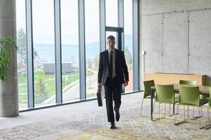 A determined businessman in a black suit confidently walks through the office, embodying professionalism and focus as he heads towards new challenges photo