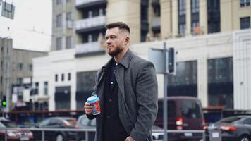 Man with coffee cup outdoor. Young businessman walking through city street and holding takeaway coffee video