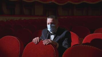 Theater after pandemic of covid-19. Man in medical mask sits alone in empty hall with red seats video