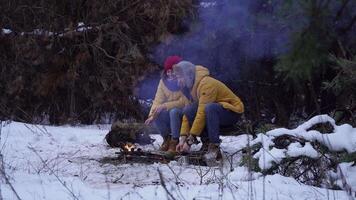 Young man and woman near a campfire in the forest in winter. Tourists travel together. The guys are cheerful and happy. Travel and adventure concept. video