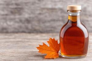 Maple syrup bottle and autumn leaf on wooden table photo