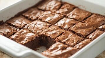 Baking dish containing an even layer of brownies, with a corner piece partially removed, photorealistic food photo