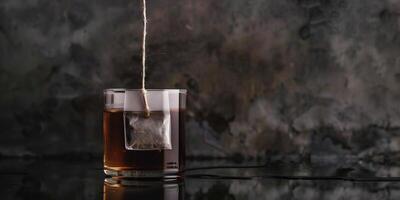Black tea teabag submerged in a glass cup of water with the string hanging over the side, gastronomy photography photo