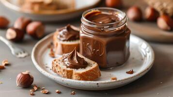 Glass jar of hazelnut spread with dollop on slice of bread on white plate, gastronomy photography photo
