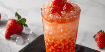 Glass filled with strawberry-flavored liquid, ice, and white tapioca pearls at the bottom, food setting photo